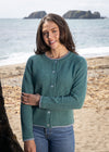 Woman wearing a green sweater on a beach with ocean and rocks in the background