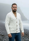 Man wearing a beige knitted cardigan standing on a rocky beach with foggy mountains in the background