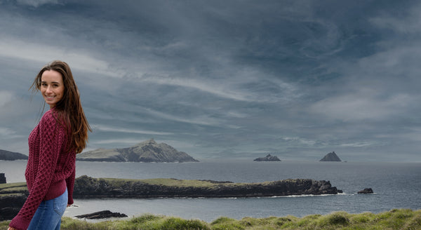 Woman in a red sweater standing on a grassy area with a scenic view of the ocean and islands.