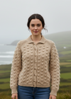 Woman wearing a beige textured cardigan standing in a scenic outdoor setting with mountains and mist.
