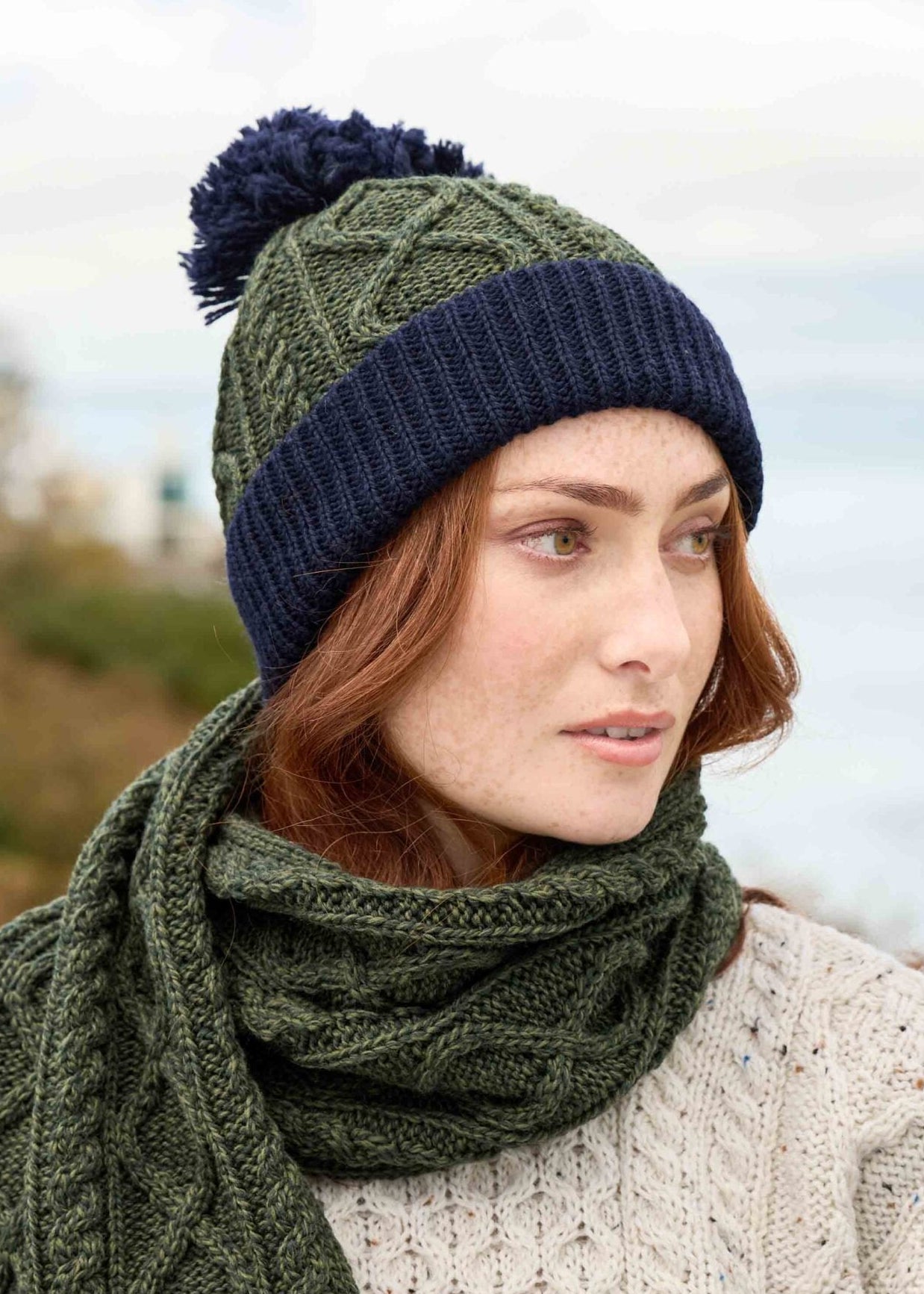 Woman wearing a green and navy knit hat and scarf with a blurred natural background