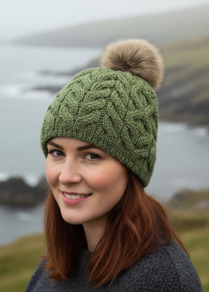 Green knitted beanie with a fur pom-pom on a white background