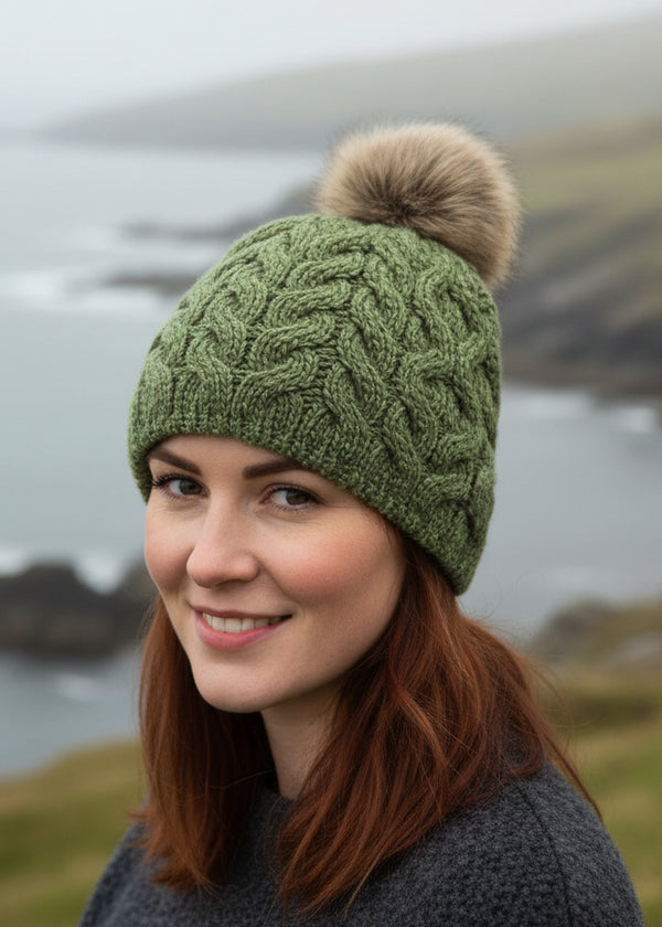 Green knitted beanie with a fur pom-pom on a white background