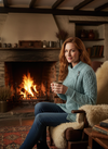 Woman wearing Aqua cardigan by fireplace in Irish cottage