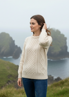 Woman wearing a cream sweater standing on a grassy hill with a scenic background