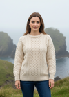 Woman wearing a cream sweater standing in front of a scenic landscape with cliffs and water.