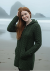 Woman wearing a green knitted coat on a beach with mountains in the background