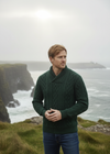 Man wearing a green sweater standing on a cliff overlooking the ocean.