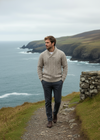 Man in a sweater standing on a coastal path with ocean and cliffs in the background