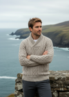 Man wearing a beige knitted sweater standing on a rocky outcrop with ocean and cliffs in the background