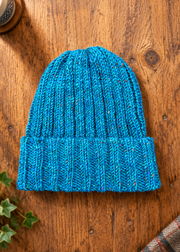 100% Donegal wool turn-up beanie hat in blue on a rustic wooden table