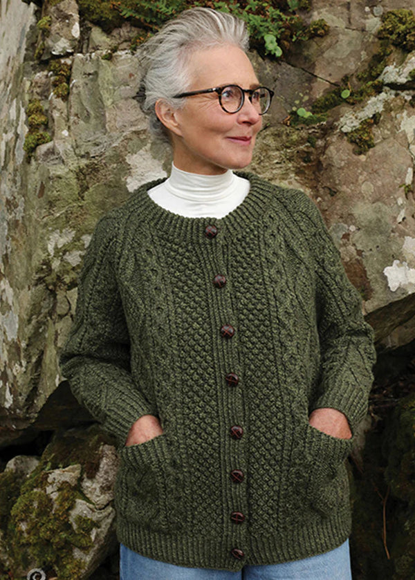 Woman wearing a green aran knitted cardigan in front of a stone wall.