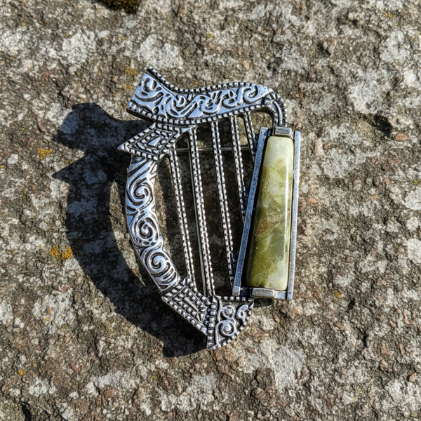 Silver harp-shaped brooch with a green stone on a textured stone surface