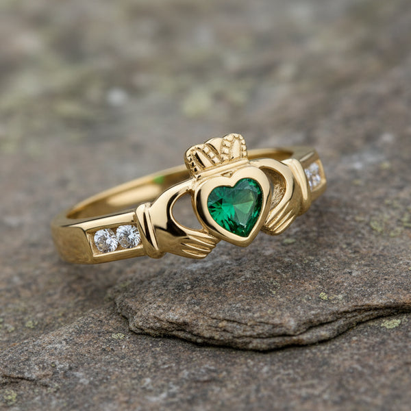 Gold claddagh ring with a green gemstone and diamonds on a white background